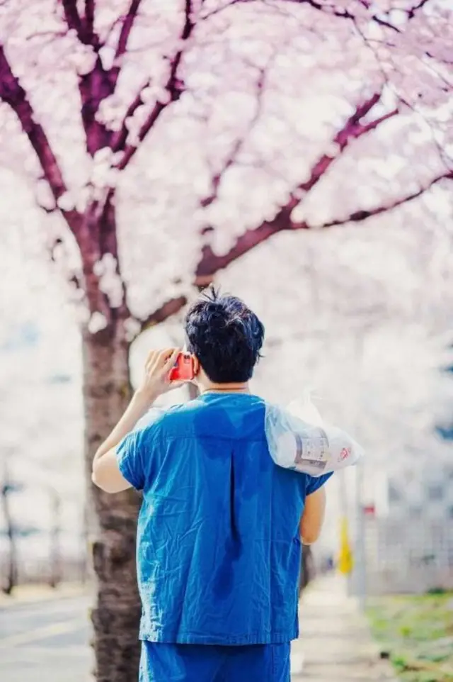 벚꽃 아래 등이 땀으로 젖은 의료진이 컵라면을 들고 서있다. 이 사진은 '코로나 19 현장 스토리 공모전'에서 최우수상인 보건복지부 장관상을 수상했다