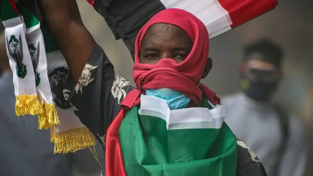 A man with a flag draped around his back holds his arm in the air