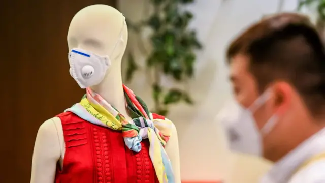 A man in face masks walk pass a mannequin wearing a mask