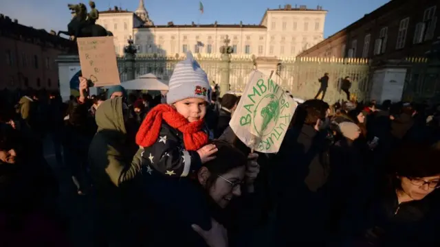 A woman holds a baby on her shoulders at a climate change protests in Italy
