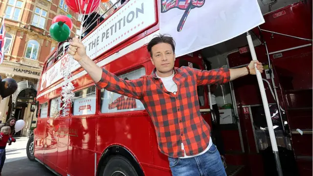 Jamie Oliver segurando balões, próximo a um ônibus