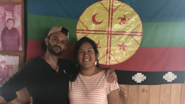 Maria e Danielpixbet whindersson nunesfrente a uma bandeira mapuche