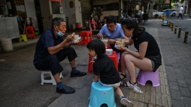 Una familia con mascarillas come junto a un puesto en Wuhan, en la provincia central china de Hubei.