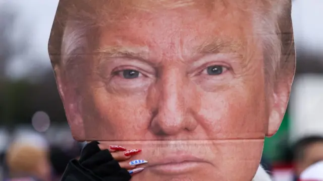 Mujer lleva pancarta con rostro de Trump.