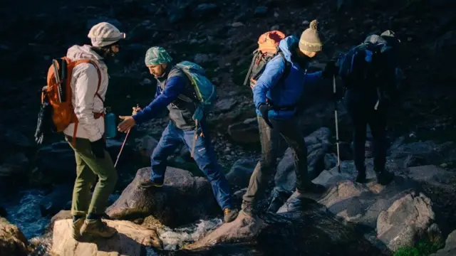 Quatro homens fazendo caminhada com equipamentos em área rochosa