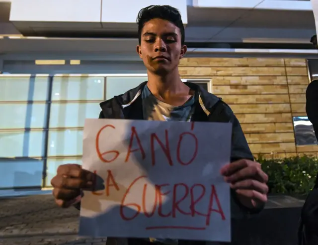 Jovem com cartazgoias e coritiba palpitesque se lê "Ganhou a Guerra"