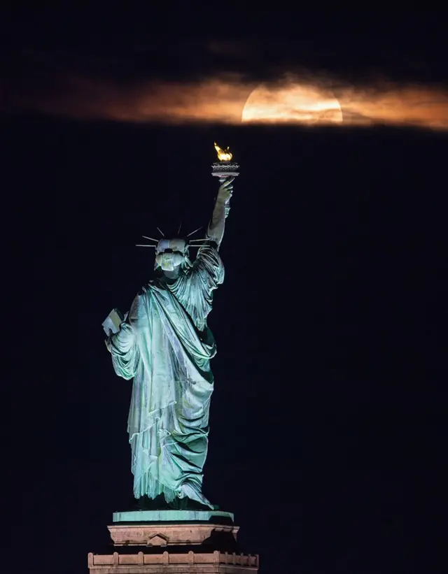 The Statue of Liberty in New York seemingly looks towards the rising moon