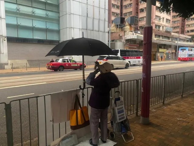 A woman is seen from behind demonstrating in front of a large office building