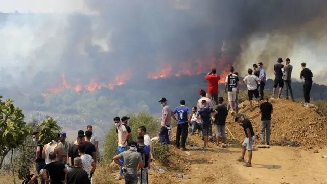 Personas ven cómo avanza el incendio en Argelia.