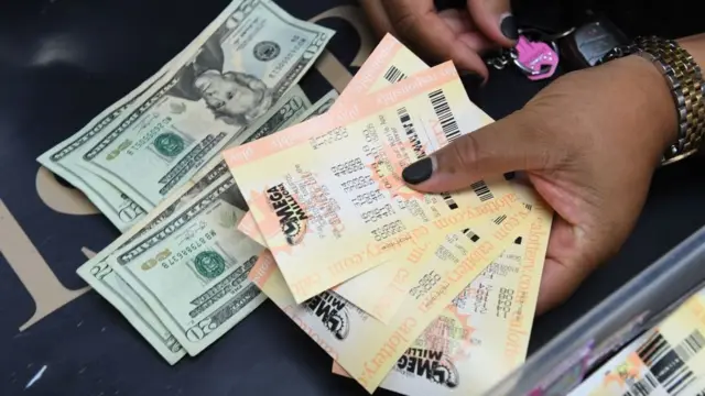Manos de una mujer con dólares y boletos de lotería.