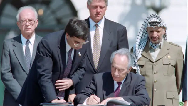 अमरीकी राष्ट्रपति कार्यालय ह्वाइट हाउस में इसराइली प्रधानमंत्री यित्ज़ाक राबिन, अमरीकी राष्ट्रपित बिल क्लिंटन, पीएलओ प्रमुख यासिर अराफ़ात की मौजूदगी में 1993 में ऑस्लो समझौते पर दस्तख़त करते इसराइली प्रधानमंत्री शिमोन पेरेज़.