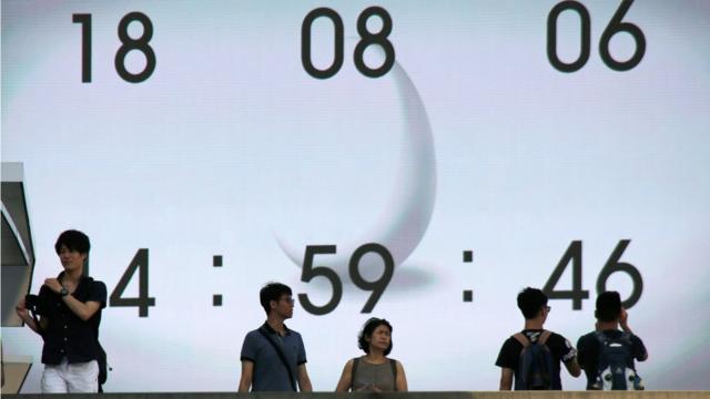 Pessoas passam em frente a relógio digital em rua do Japão