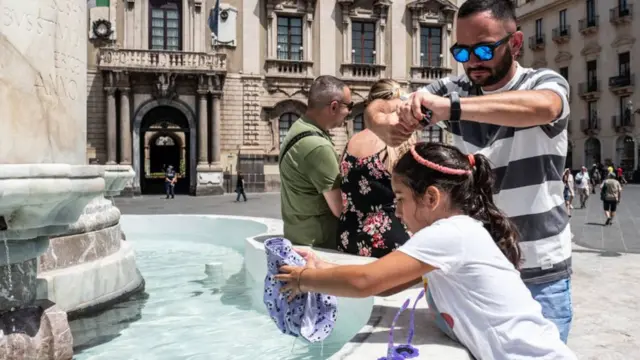 Une petite fille mouille son chapeau parce qu'il fait trop chaud dans la fontaine aux éléphants de la Piazza Duomo pendant que son père se mouille la tête le 15 juillet 2023 à Catane, en Italie.