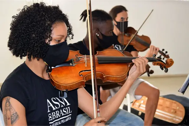 Três jovens (Samuel no centro) tocam violino juntos