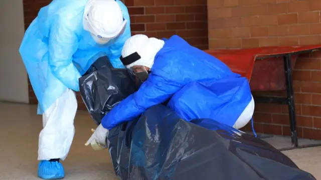 Personal sanitario con un cadáver en una bolsa.