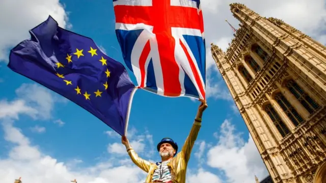 Un hombre sostiene la bandera de Reino Unido y la UE frente al parlamento británico