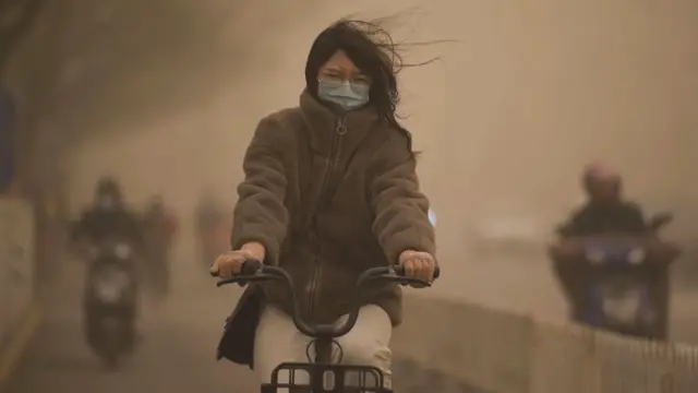 Mulher pedalando com máscara, olhos fechados e com céu turvo ao redor dela