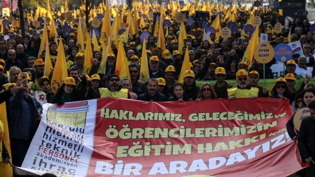Dezenas de professores e pesquisadores da Turquia são vistos em rua de Ancara, com capacetes e bandeiras amarelas, além de com cartaz dizendo: "Estamos juntos pelo direito de nossos estudantes à educação"
