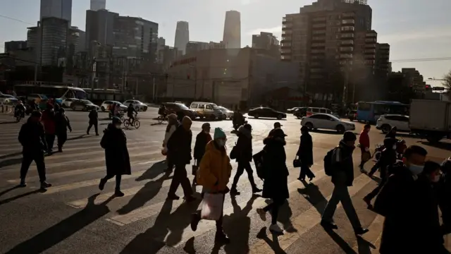 People cross a street during morning rush hour in front of the skyline of the central business district (CBD) in Beijing, China December 15, 2020.