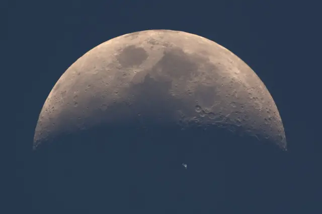 The International Space Station (ISS) whizzes across the dusky face of the moon