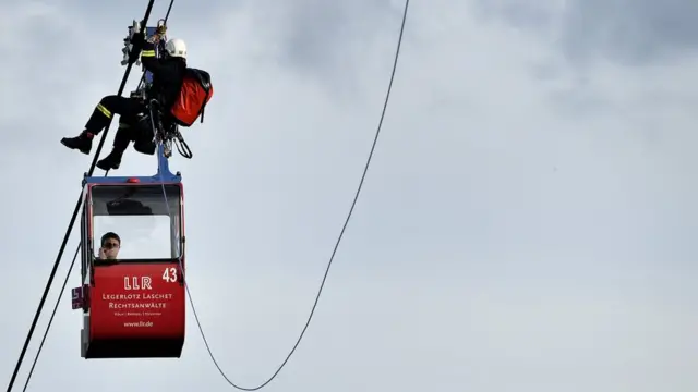 German fire crews evacuate dozens of passengers from suspended cable cars that run over the river Rhine after a gondola ran into a support pillar in Cologne, Germany, 30 July 2017