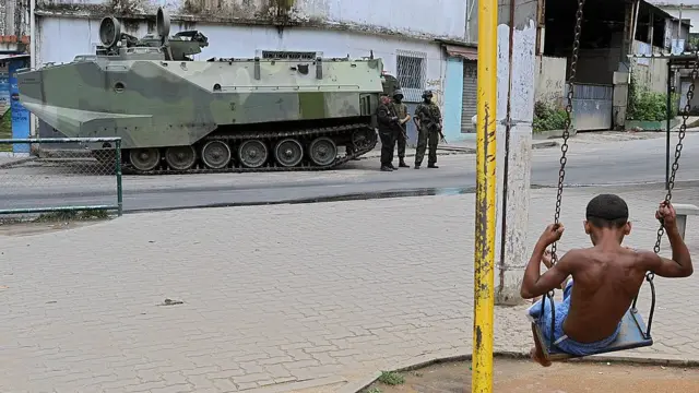 Garoto num balanço observa tanque da Marinha no Riogran cassinoJaneiro