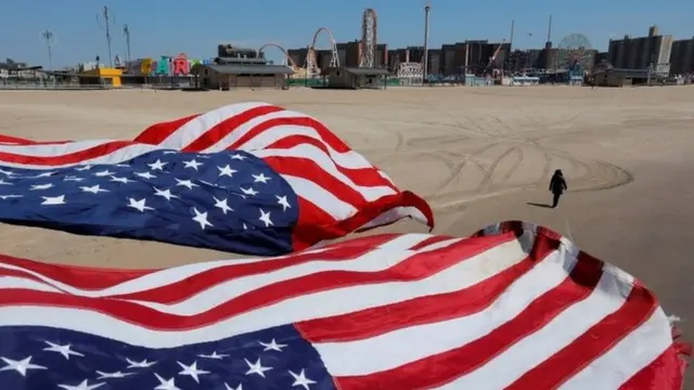 A person walks along the sand under flags of the United States of America at the Coney Island beach