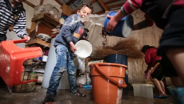 طفل يساعد بإزالة المياه من الخيمة التي طافت في فصل الشتاء (يناير 2018) في مخيم في منطقة البقاع.