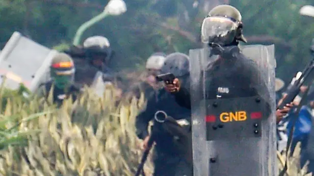 Un funcionario de la Guardia Nacional Bolivariana apunta con un arma de fuego a los manifestantes.