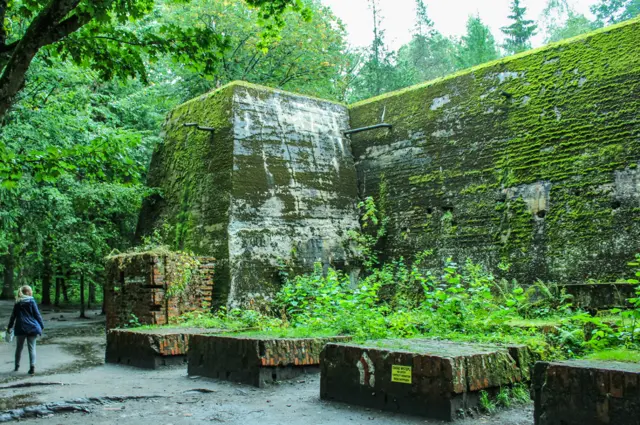 Turista observa monumento coberto por floresta no Wolfsschanze