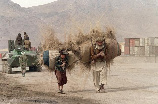 Afghan man and youth haul fire wood on their shoulders past Afghan regular army armoured personnel carrier 15 February 1989 on the Salang Highway near Kabul. Over 100,000 Soviet troops have left the country after nine years's military committment.