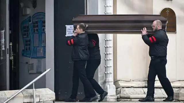 Навальний жасади солинган тобутни кўтариб бораётган дафн маросими хизматини кўрсатадиган ширкатнинг тўрт эркак ходими