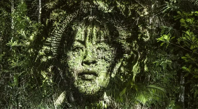 A woman's face is projected on to the Brazilian rainforest canopy