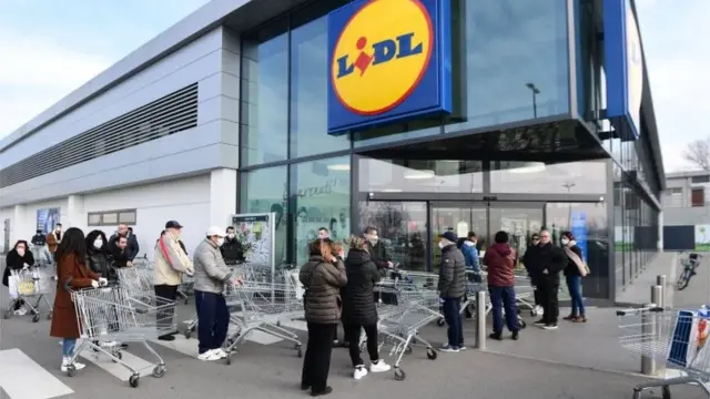 Residents wearing respiratory mask wait to be given access to shop in a supermarket in small groups of forty people on February 23, 2020 in the small Italian town of Casalpusterlengo