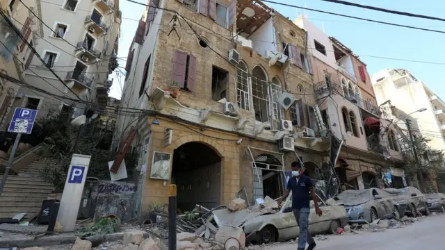 A man wearing a protective face mask walks past damaged buildings