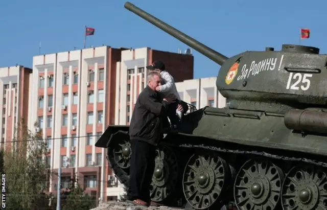 A man helps a child climb down from a tank, exhibited as part of a display