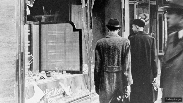 Des Allemands passent devant les vitres brisées d'un magasin au lendemain de la Nuit de Cristal, une nuit qui a montré au monde entier à quel point l'Allemagne devenait dangereuse pour les Juifs
