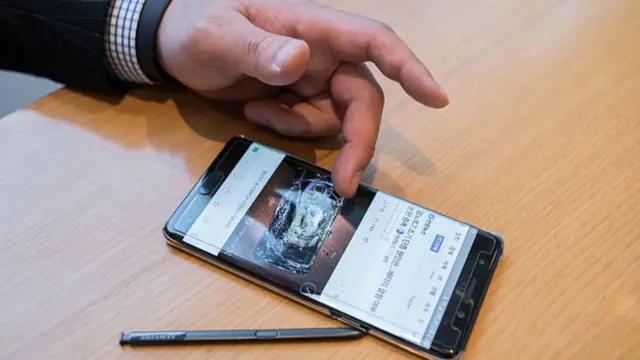 Un client dans une boutique montrant sur son téléphone de la même marque un Galaxy Note 7 détruit par explosion