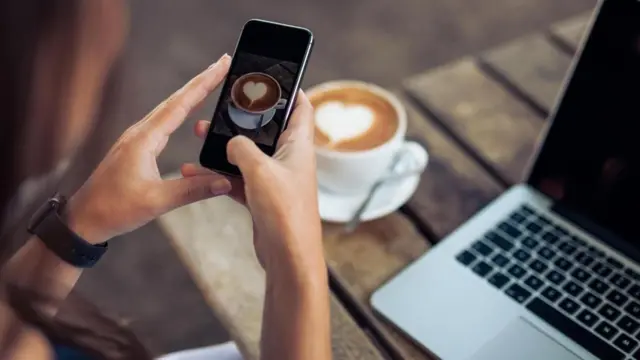 شابة تلتقط صورة لفنجان قهوة على مكتبها