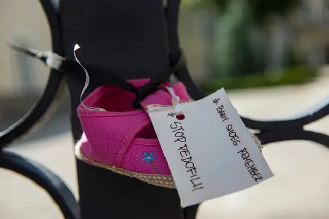 Sebuah sepatu bayi dengan kartu bertuliskan '#StopPedofili'