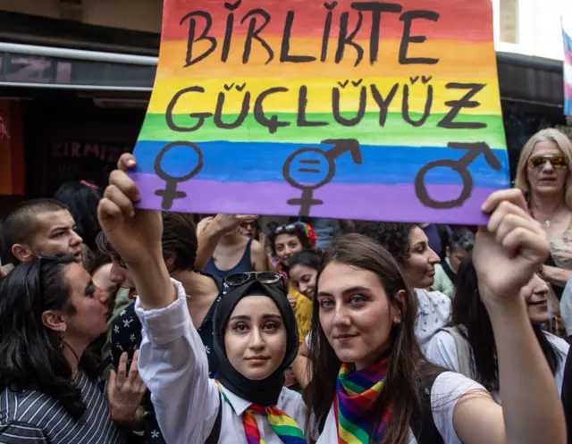 "birlikte güçlüyüz" pankartı tutan biri türbanlı iki kadın