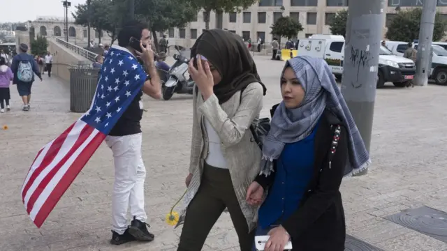 Palestinian women walk next to a man wearing a US flag outside the Old City, Jerusalem, 13 May