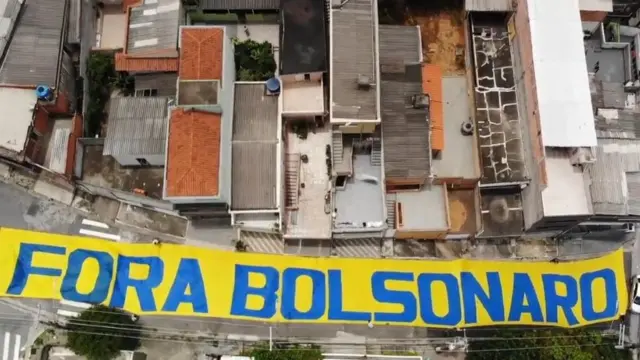 Faixa amarela colocada na rua e vista do alto diz 'fora bolsonaro'jogo grátis para jogar agoraazul; ao lado, telhadosjogo grátis para jogar agoracasas