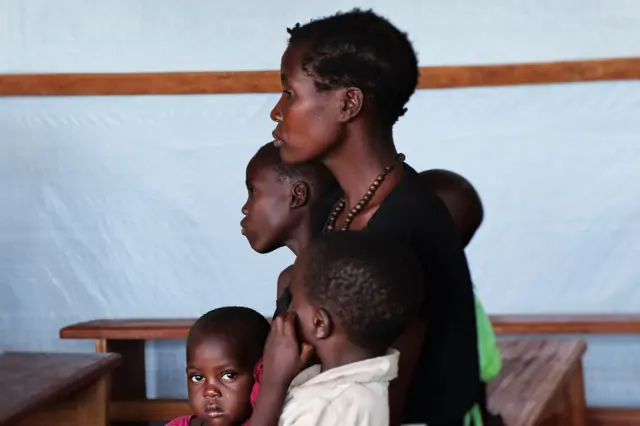 Une mère assise dans un centre de santé provisoire avec ses enfants malades en attente des soins.