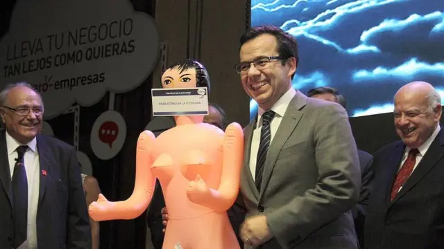 El ministro de Economía, muy sonriente mientras enseña una muñeca inflable con un letrero de "Para estimular la economía"