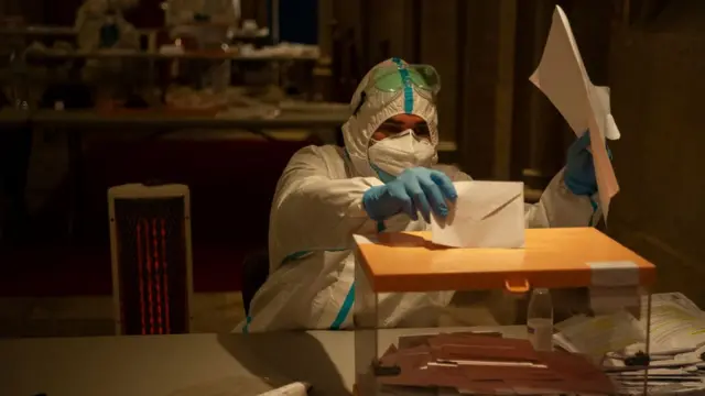 Выборы в Каталонии 14 февраля, сотрудник избирательного участка в защитном костюме