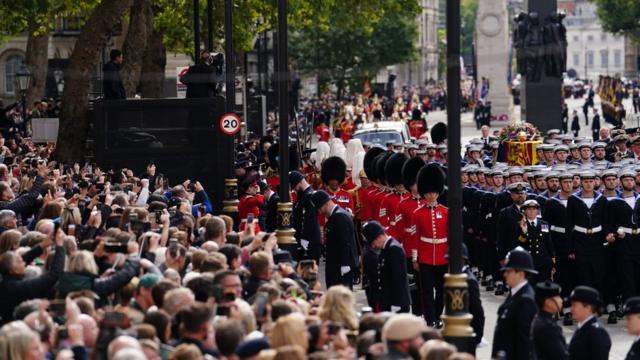 La gente se agolpa y hace fotos al paso de los restos mortales de Isabel II en su último recorrido por las calles de Londres.