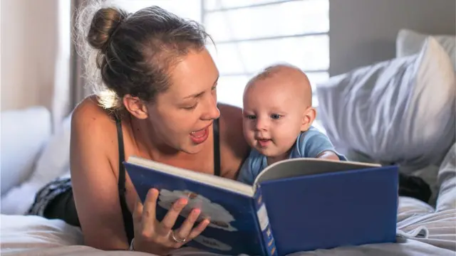 Uma mulher branca lendo um livro para um bebê