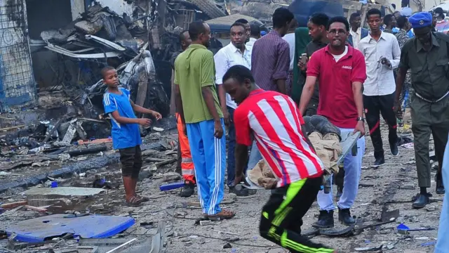 Two people dey carry pesron wey injure ontop stretcher as other people gather dey look