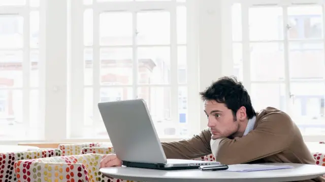 Homem debruçado na mesa olhando para laptop